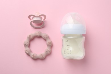 Photo of Feeding bottle with milk, pacifier and teether on pink background, flat lay