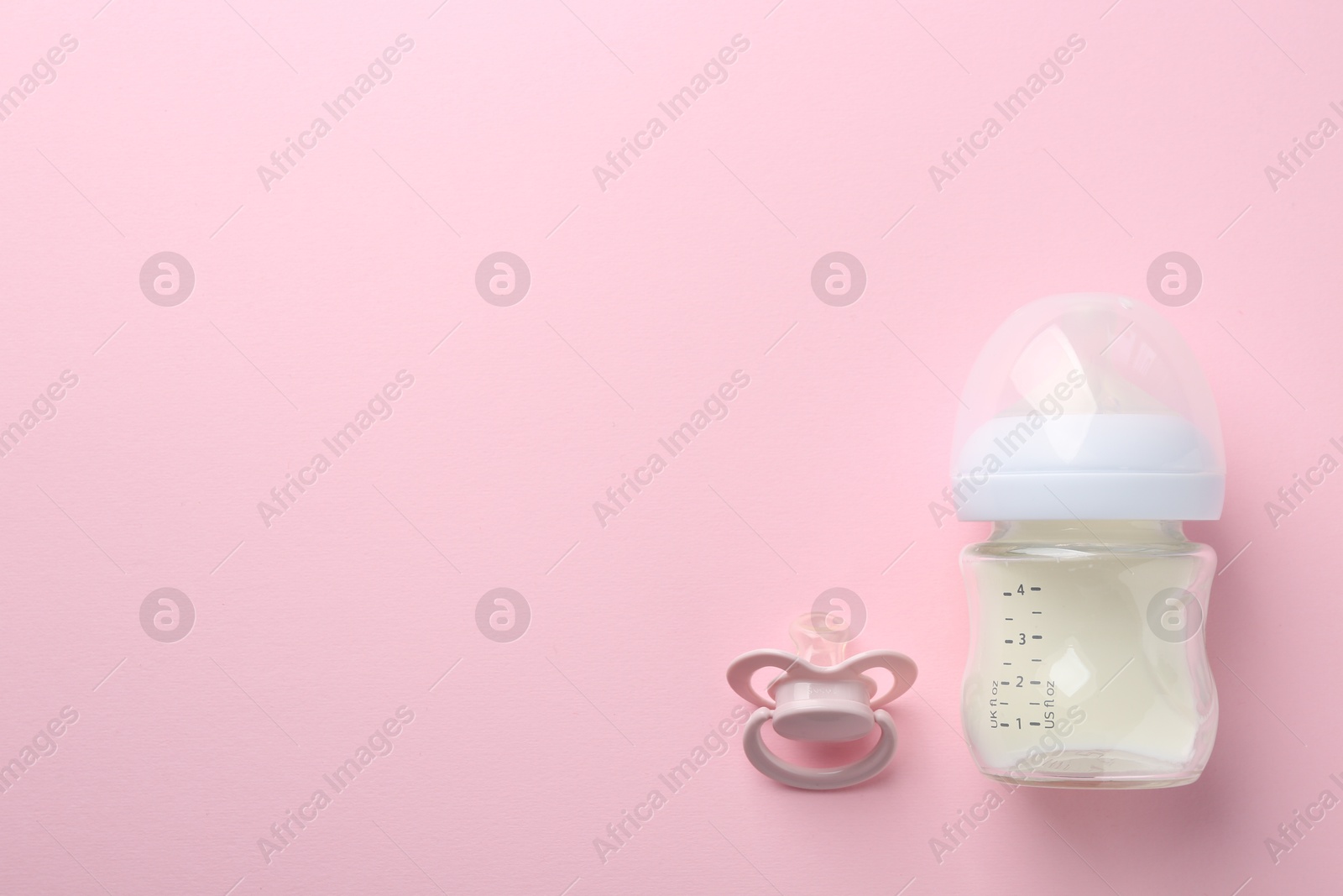 Photo of Feeding bottle with milk and pacifier on pink background, flat lay. Space for text