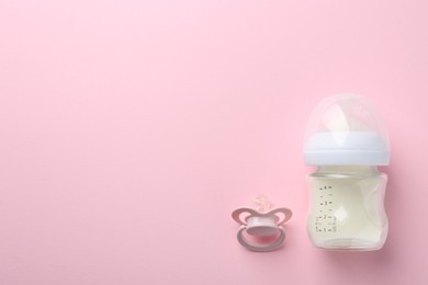 Feeding bottle with milk and pacifier on pink background, flat lay. Space for text