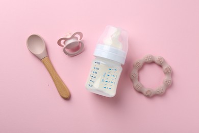 Feeding bottle with milk, spoon, pacifier and teether on pink background, flat lay