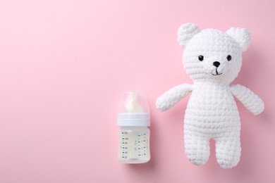 Feeding bottle with milk and toy bear on pink background, flat lay. Space for text