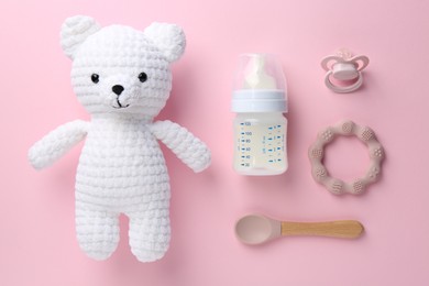 Photo of Feeding bottle with milk, spoon, pacifier, toy bear and teether on pink background, flat lay