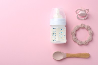 Photo of Feeding bottle with milk, spoon, pacifier and teether on pink background, flat lay. Space for text