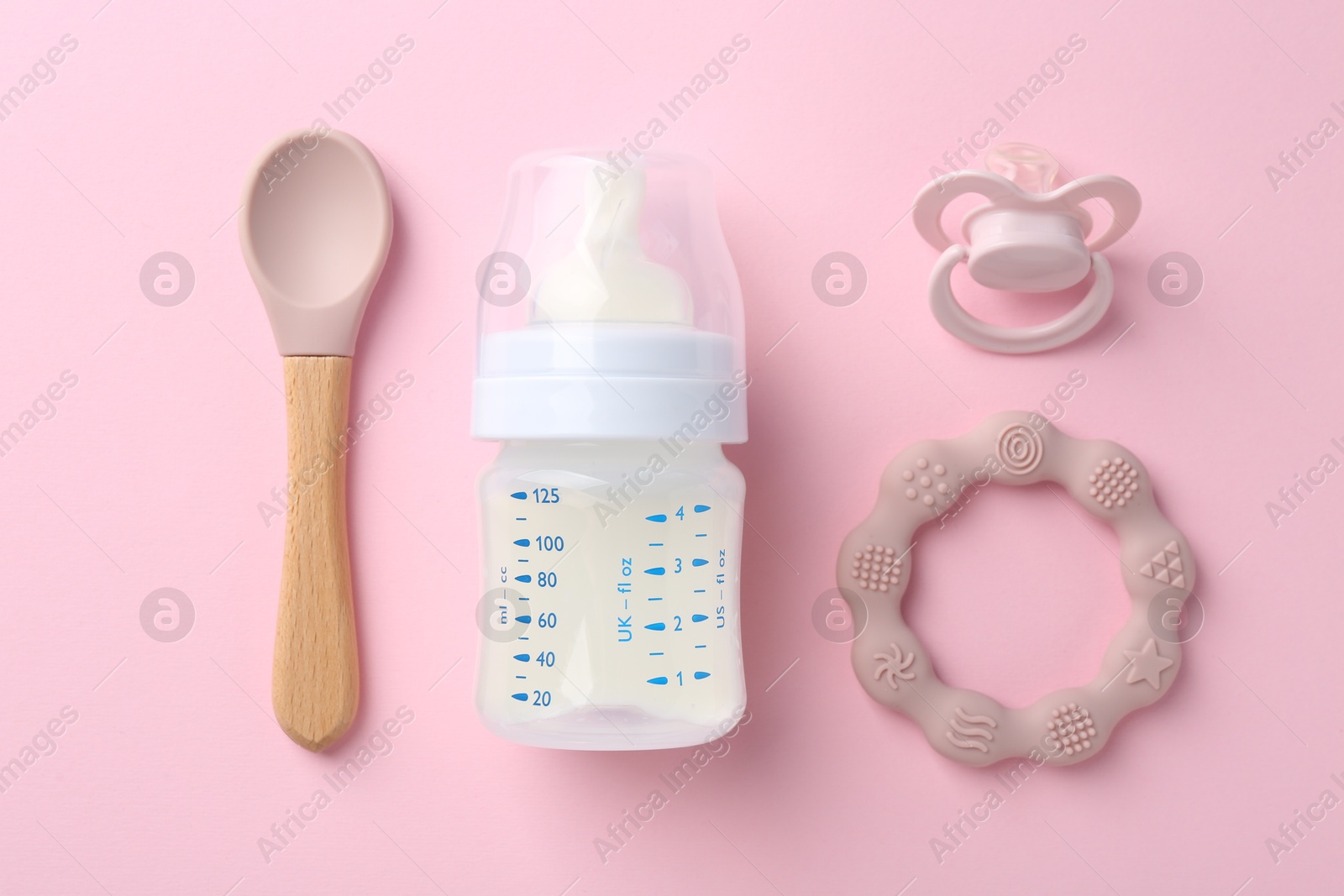 Photo of Feeding bottle with milk, spoon, pacifier and teether on pink background, flat lay