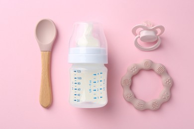 Feeding bottle with milk, spoon, pacifier and teether on pink background, flat lay