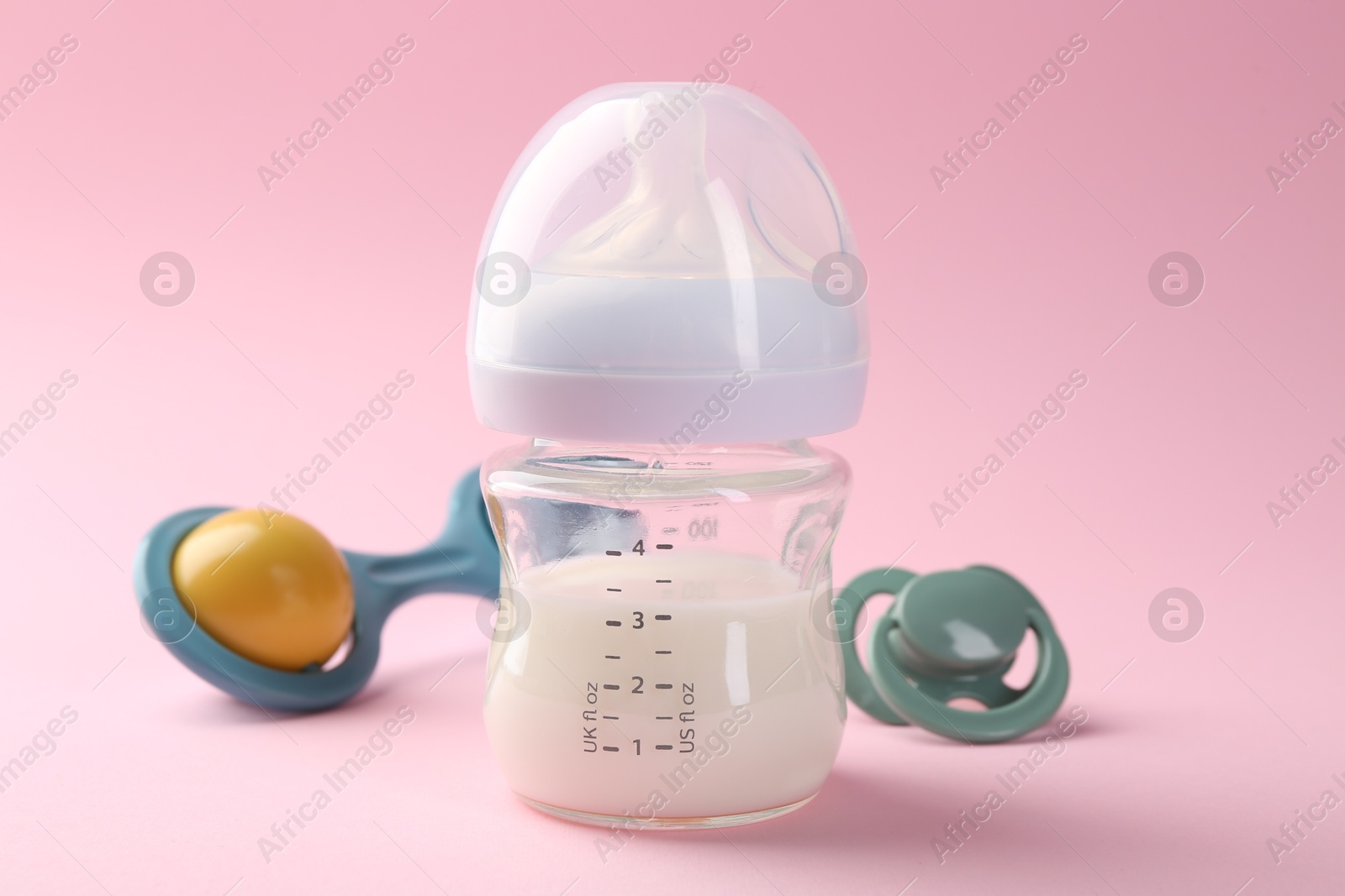 Photo of Feeding bottle with milk, pacifier and baby rattle on pink background