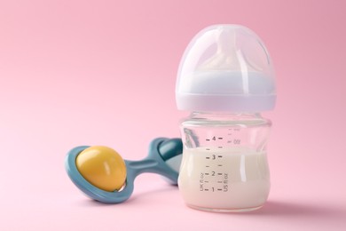 Photo of Feeding bottle with milk and baby rattle on pink background