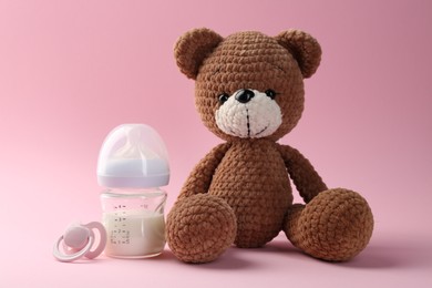 Feeding bottle with milk, pacifier and toy bear on pink background