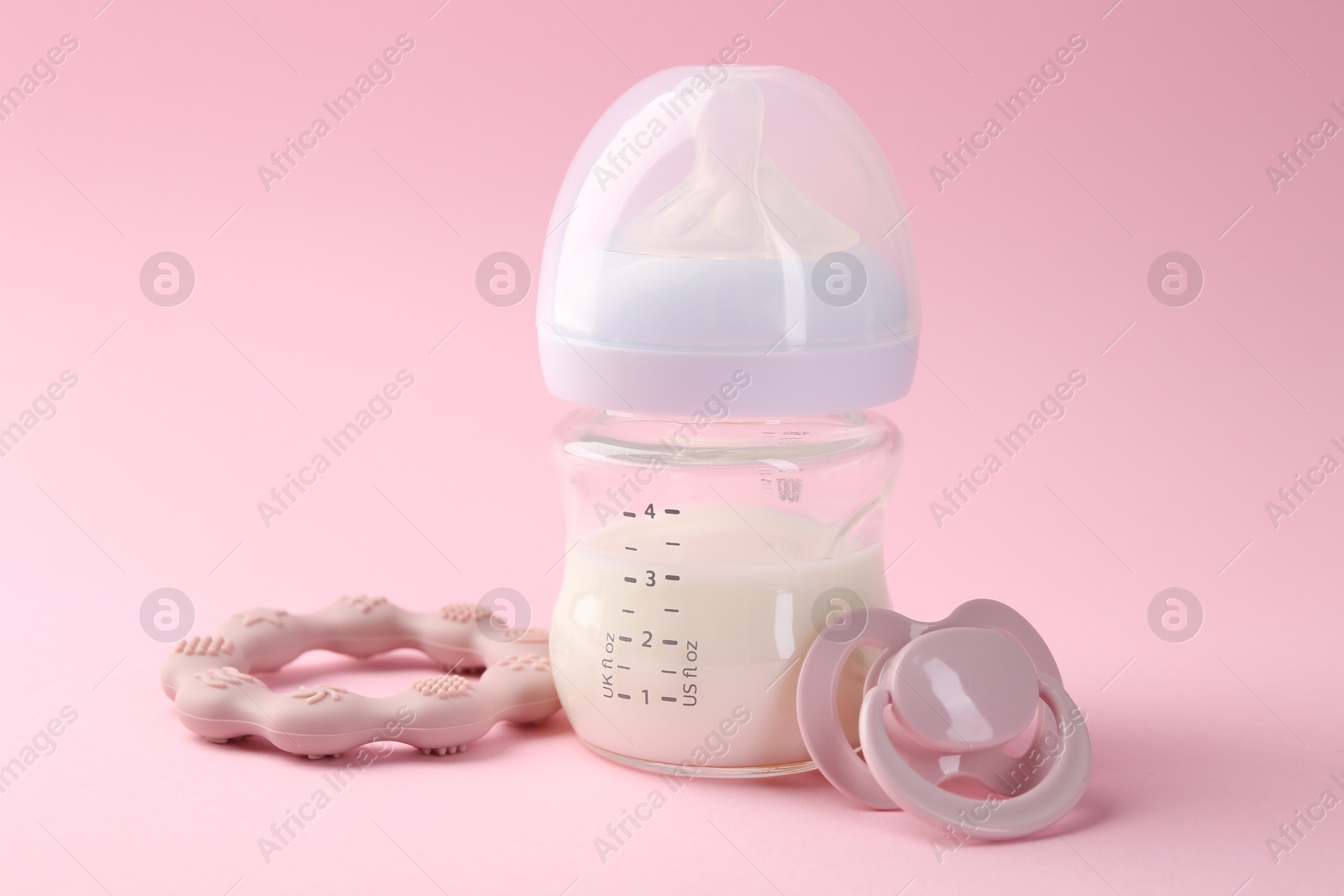 Photo of Feeding bottle with milk, teether and pacifier on pink background