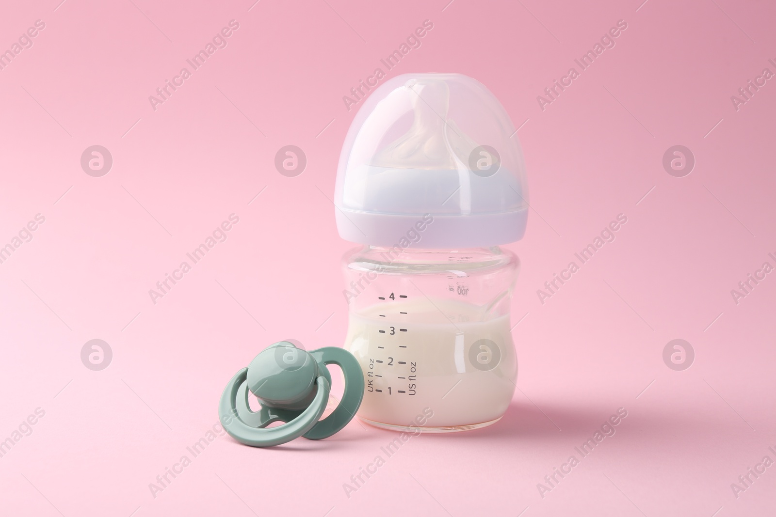 Photo of Feeding bottle with milk and pacifier on pink background