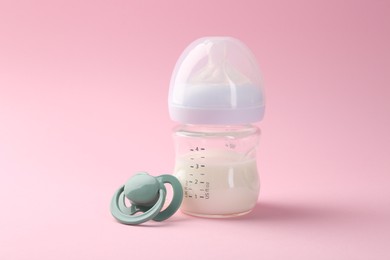 Feeding bottle with milk and pacifier on pink background