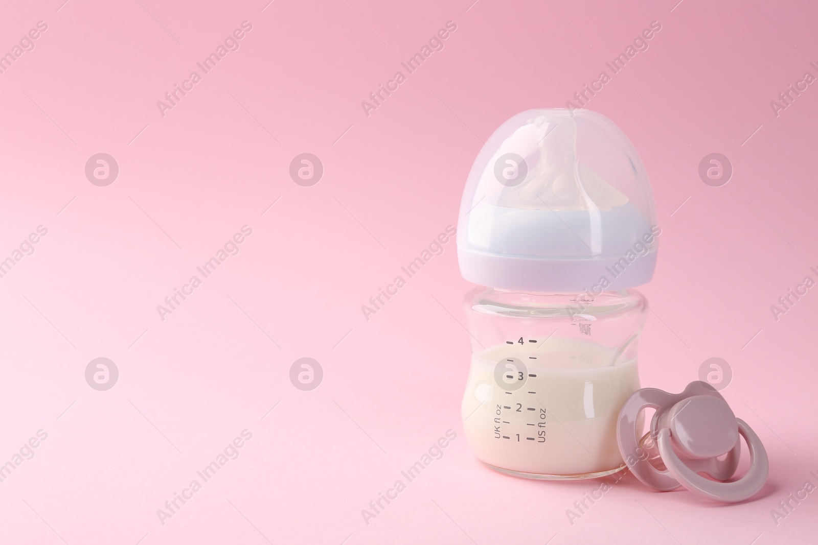 Photo of Feeding bottle with milk and pacifier on pink background, space for text