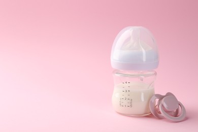 Feeding bottle with milk and pacifier on pink background, space for text