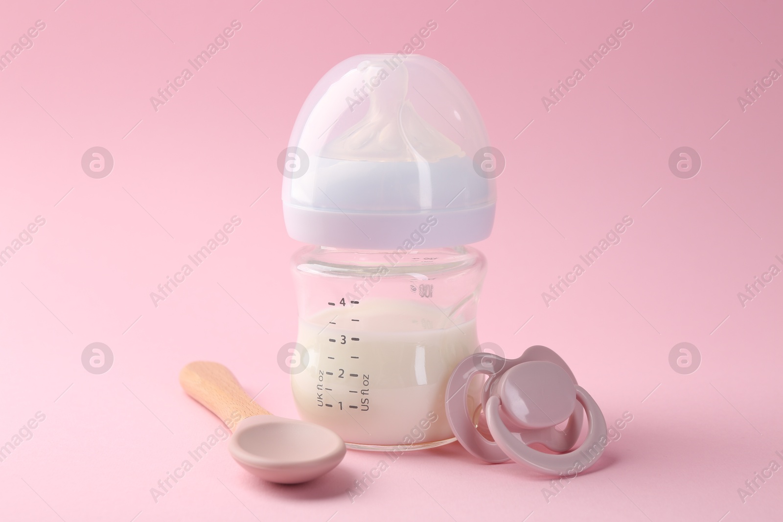 Photo of Feeding bottle with milk, spoon and pacifier on pink background