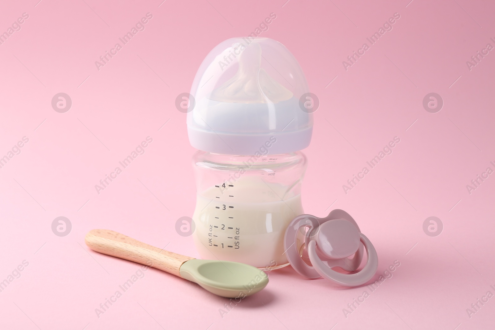 Photo of Feeding bottle with milk, spoon and pacifier on pink background