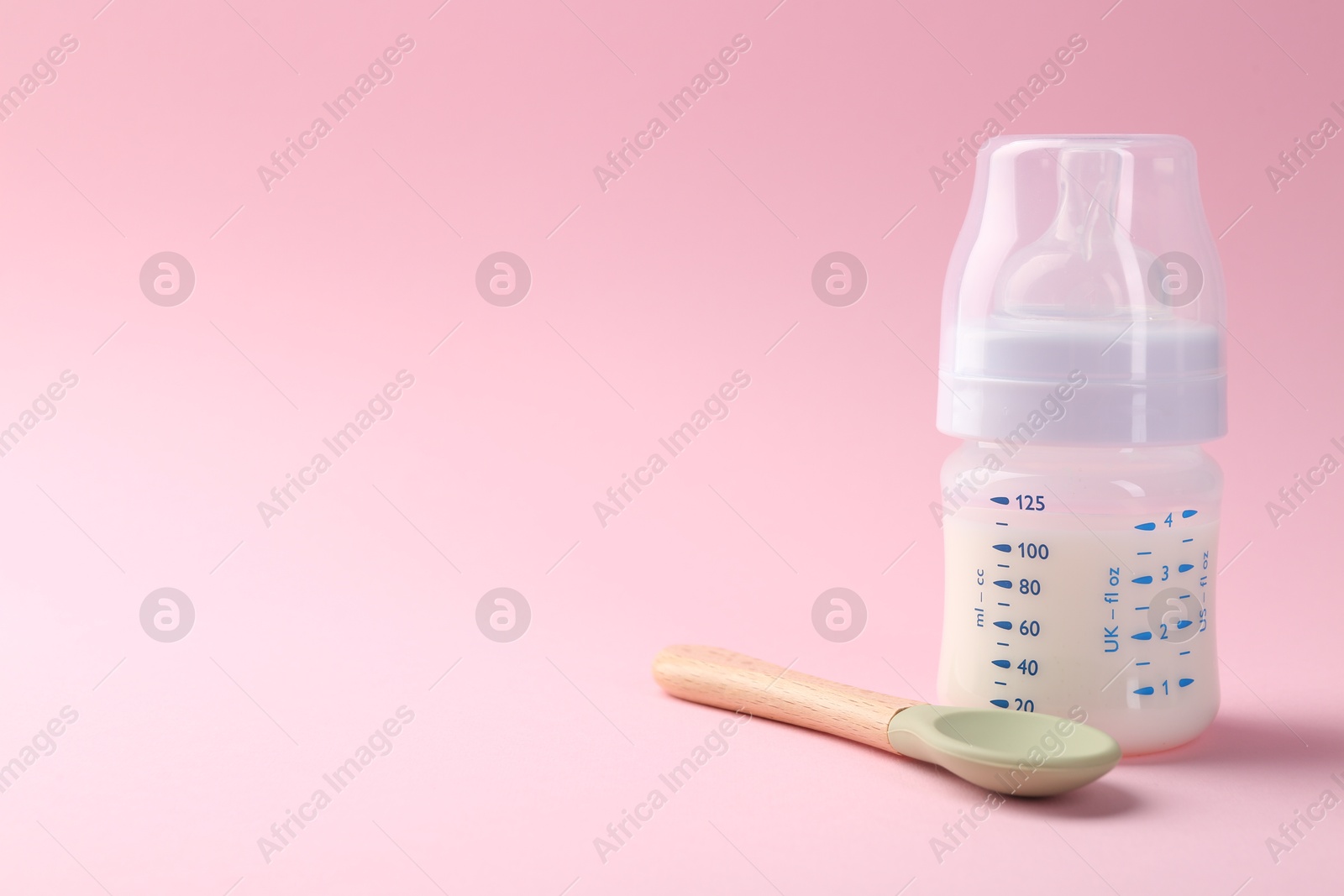 Photo of Feeding bottle with milk and spoon on pink background, space for text