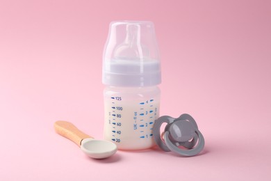 Photo of Feeding bottle with milk, spoon and pacifier on pink background