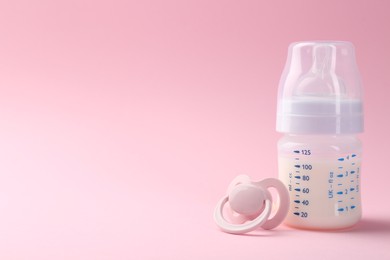 Photo of Feeding bottle with milk and pacifier on pink background, space for text