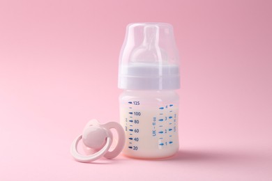 Feeding bottle with milk and pacifier on pink background