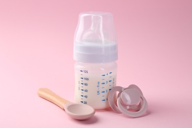 Photo of Feeding bottle with milk, spoon and pacifier on pink background