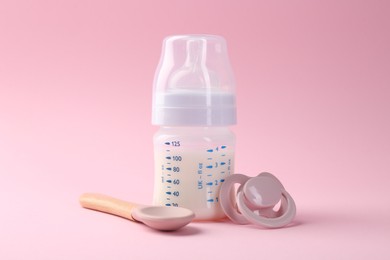 Photo of Feeding bottle with milk, spoon and pacifier on pink background