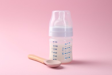 Feeding bottle with milk and spoon on pink background