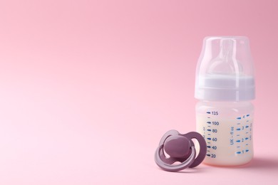 Feeding bottle with milk and pacifier on pink background, space for text