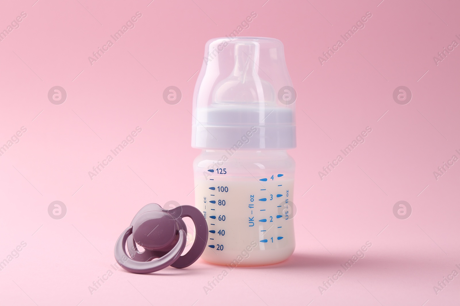 Photo of Feeding bottle with milk and pacifier on pink background