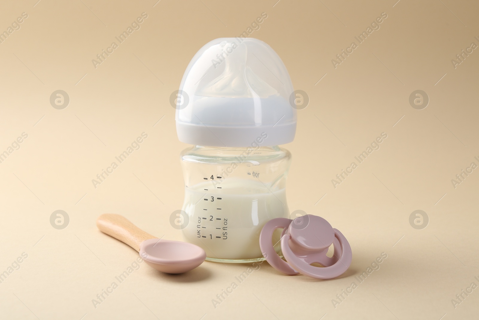 Photo of Feeding bottle with milk, spoon and pacifier on beige background