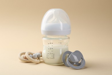 Photo of Feeding bottle with milk, teether and pacifier on beige background