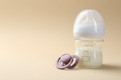 Photo of Feeding bottle with milk and pacifier on beige background, space for text