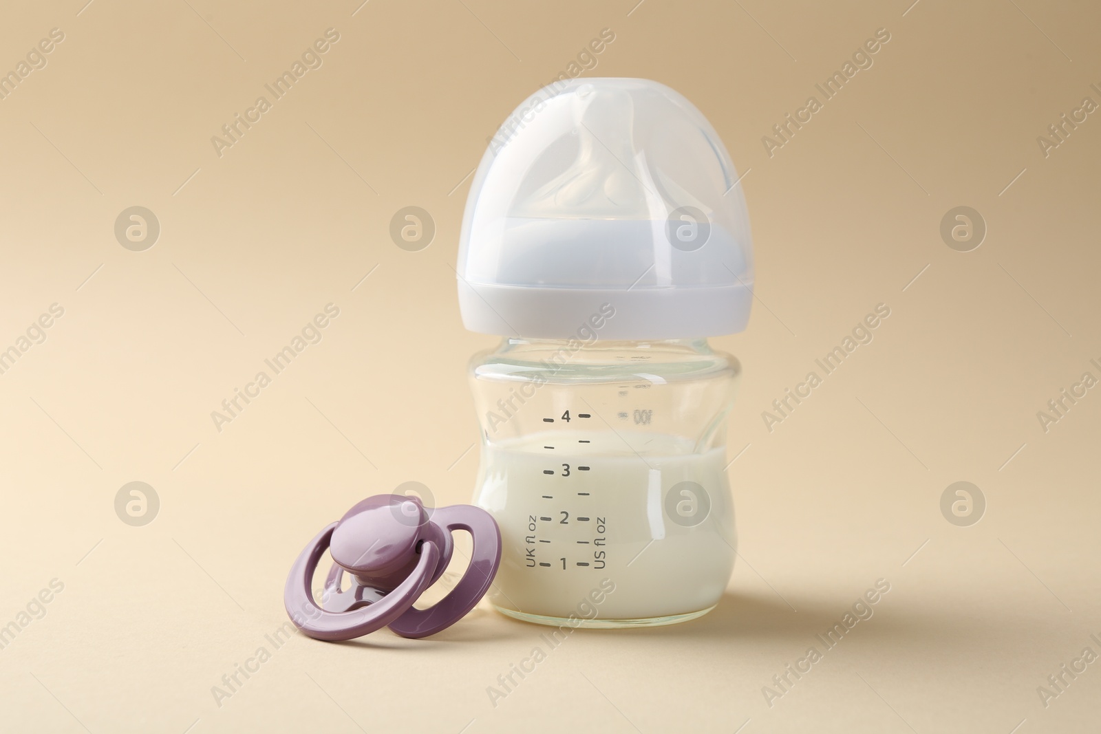 Photo of Feeding bottle with milk and pacifier on beige background