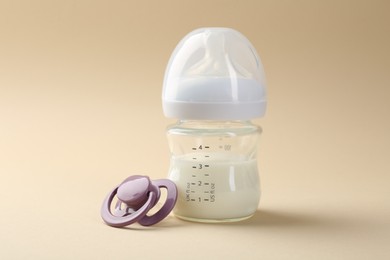 Photo of Feeding bottle with milk and pacifier on beige background