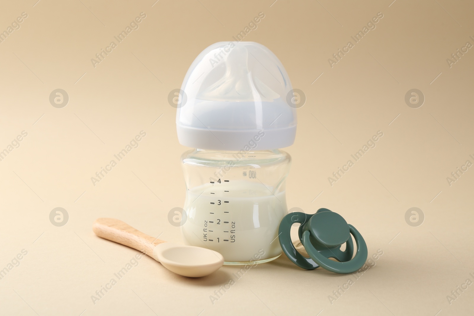 Photo of Feeding bottle with milk, spoon and pacifier on beige background