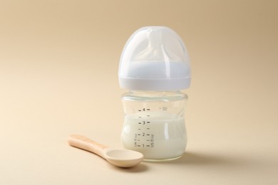 Feeding bottle with milk and spoon on beige background