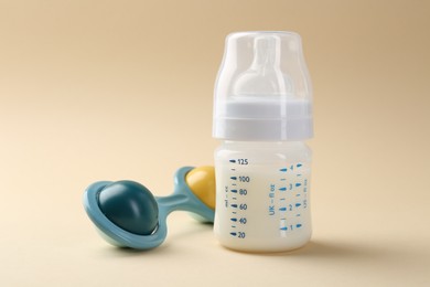 Photo of Feeding bottle with milk and baby rattle on beige background