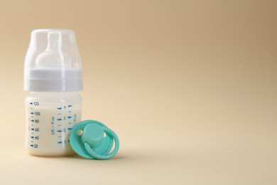 Feeding bottle with milk and pacifier on beige background, space for text