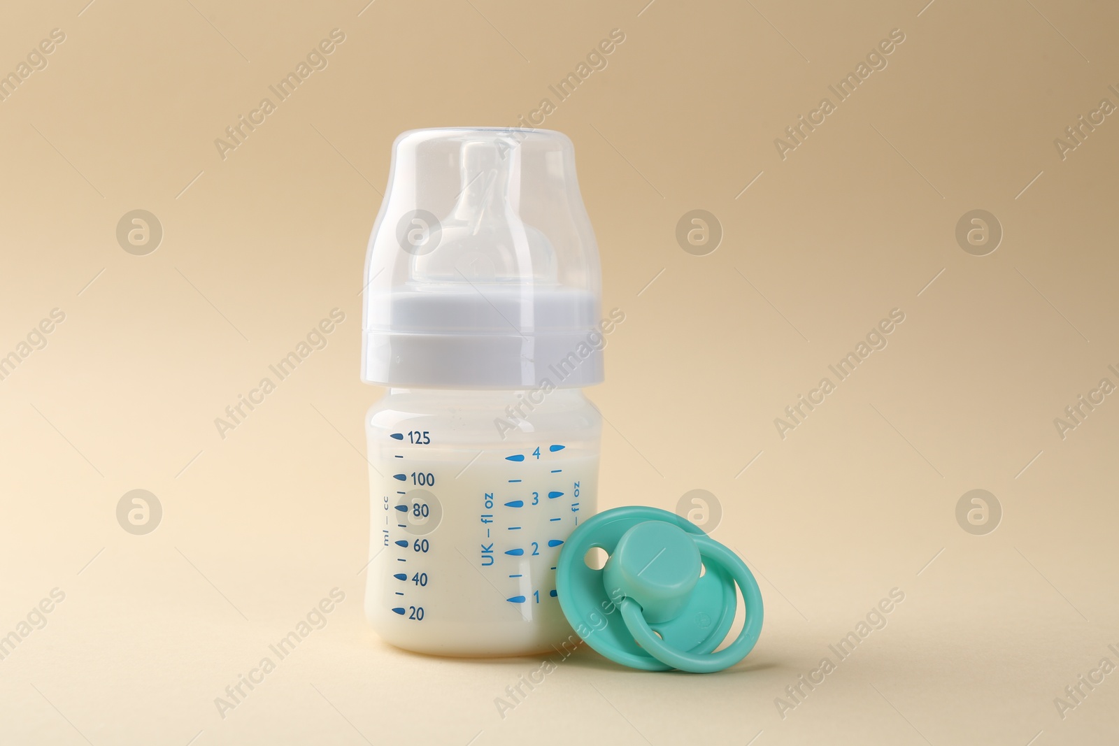 Photo of Feeding bottle with milk and pacifier on beige background