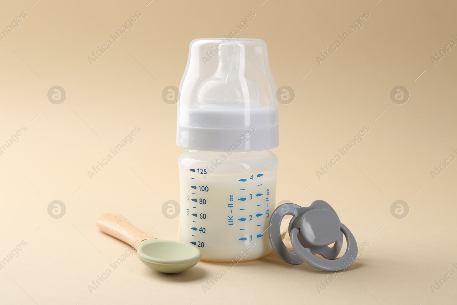 Photo of Feeding bottle with milk, spoon and pacifier on beige background