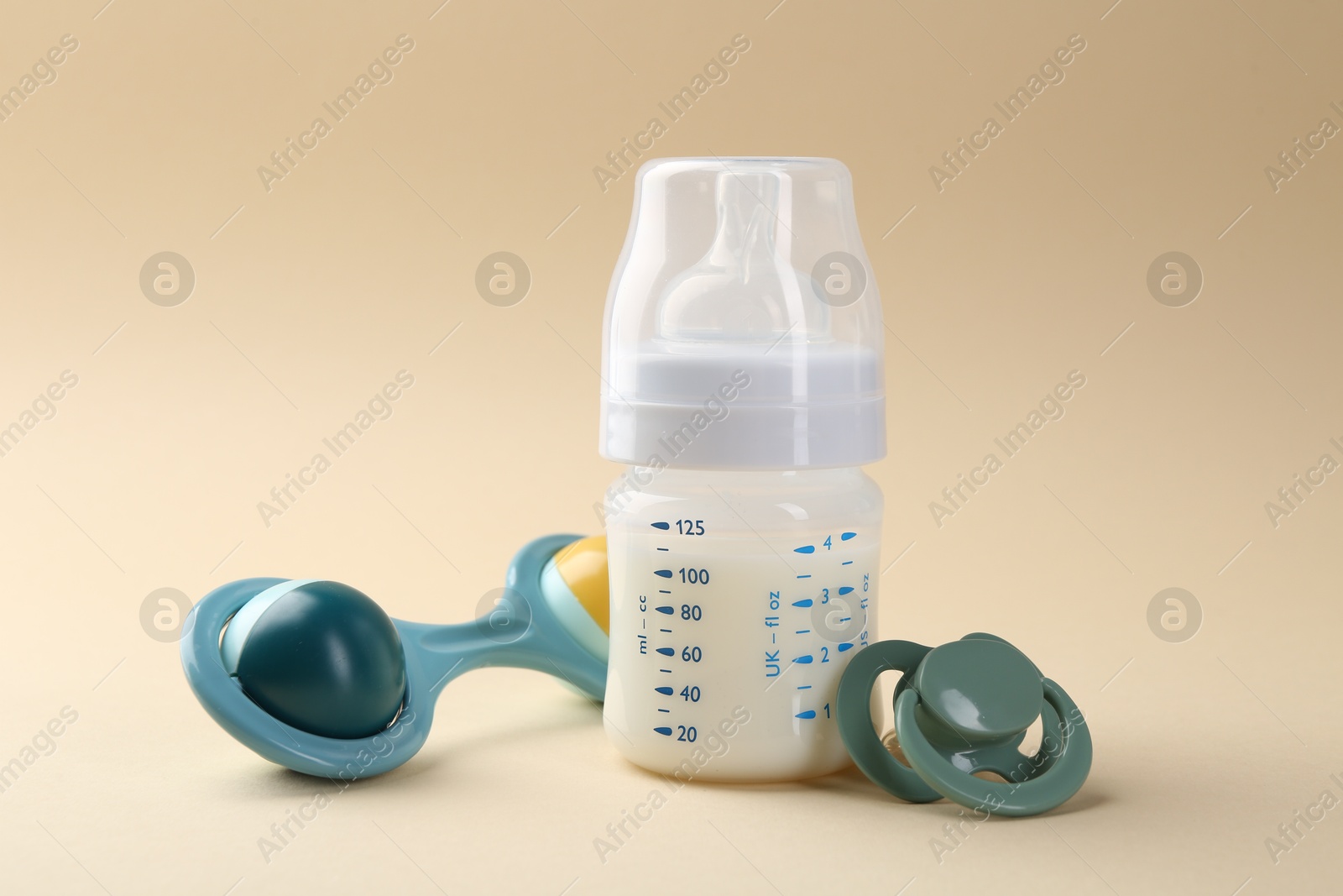 Photo of Feeding bottle with milk, pacifier and baby rattle on beige background