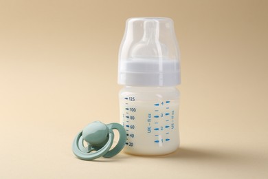 Photo of Feeding bottle with milk and pacifier on beige background