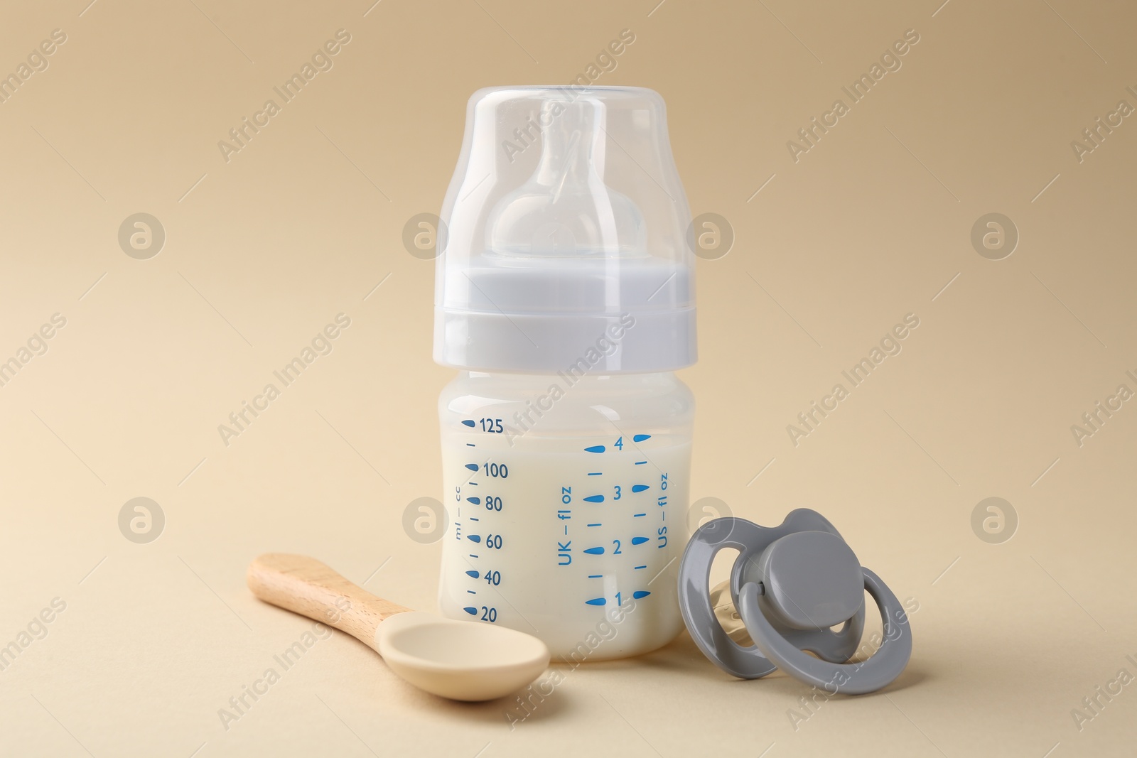 Photo of Feeding bottle with milk, spoon and pacifier on beige background