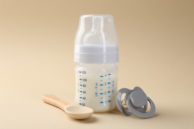 Feeding bottle with milk, spoon and pacifier on beige background