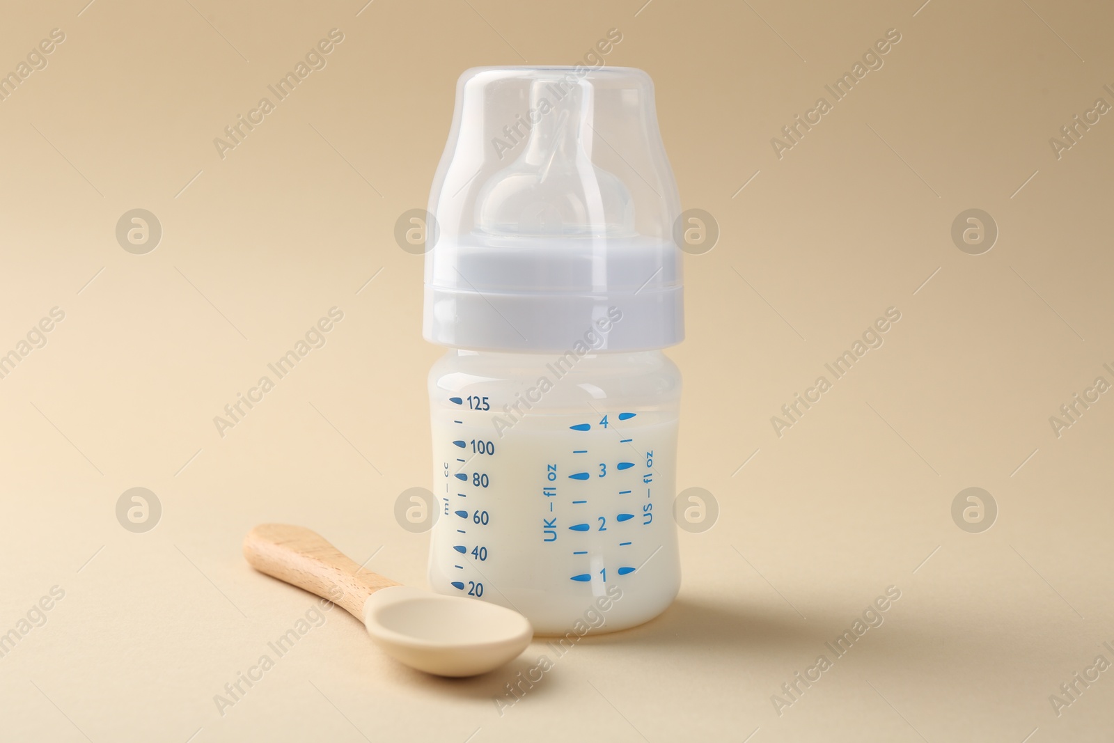 Photo of Feeding bottle with milk and spoon on beige background