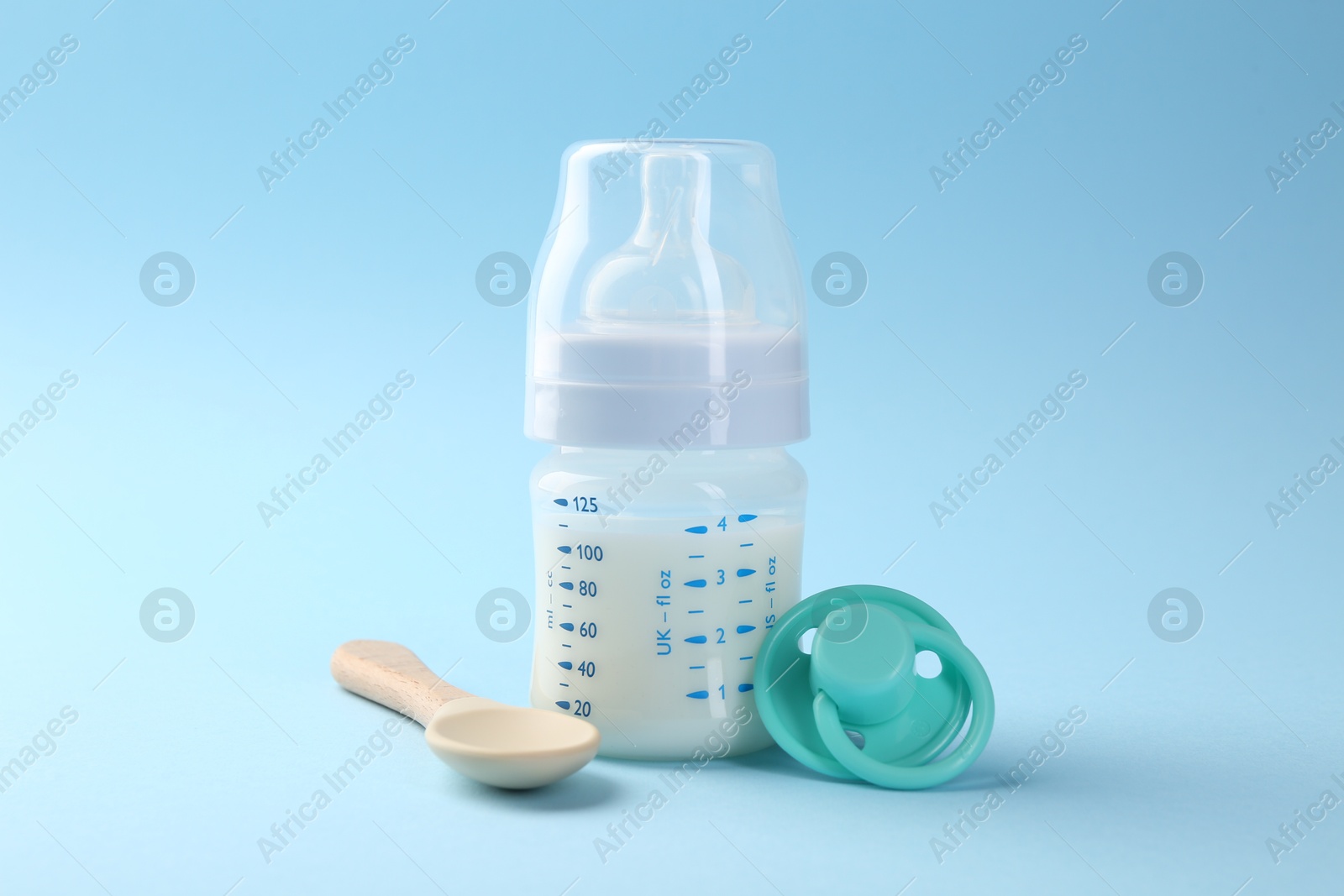 Photo of Feeding bottle with milk, spoon and pacifier on light blue background