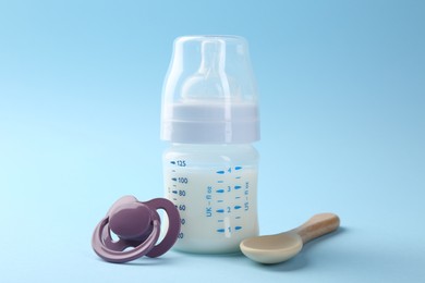 Feeding bottle with milk, spoon and pacifier on light blue background