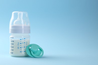 Photo of Feeding bottle with milk and pacifier on light blue background, space for text