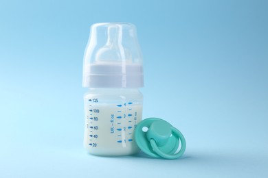 Feeding bottle with milk and pacifier on light blue background