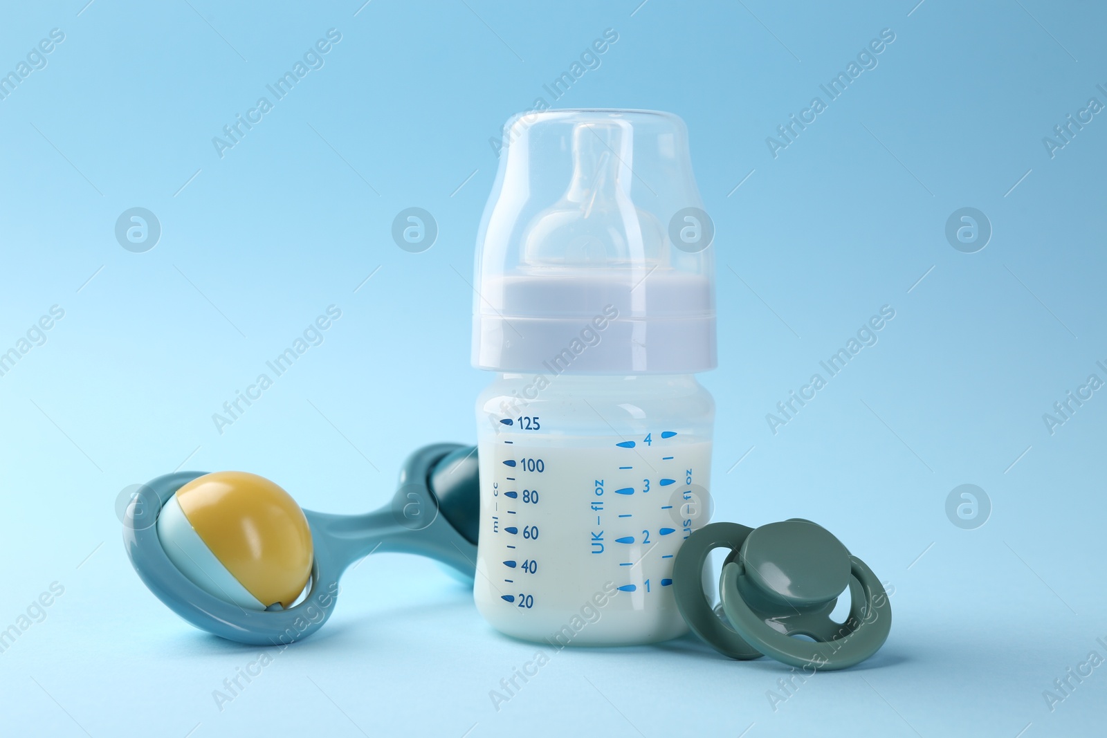 Photo of Feeding bottle with milk, pacifier and baby rattle on light blue background