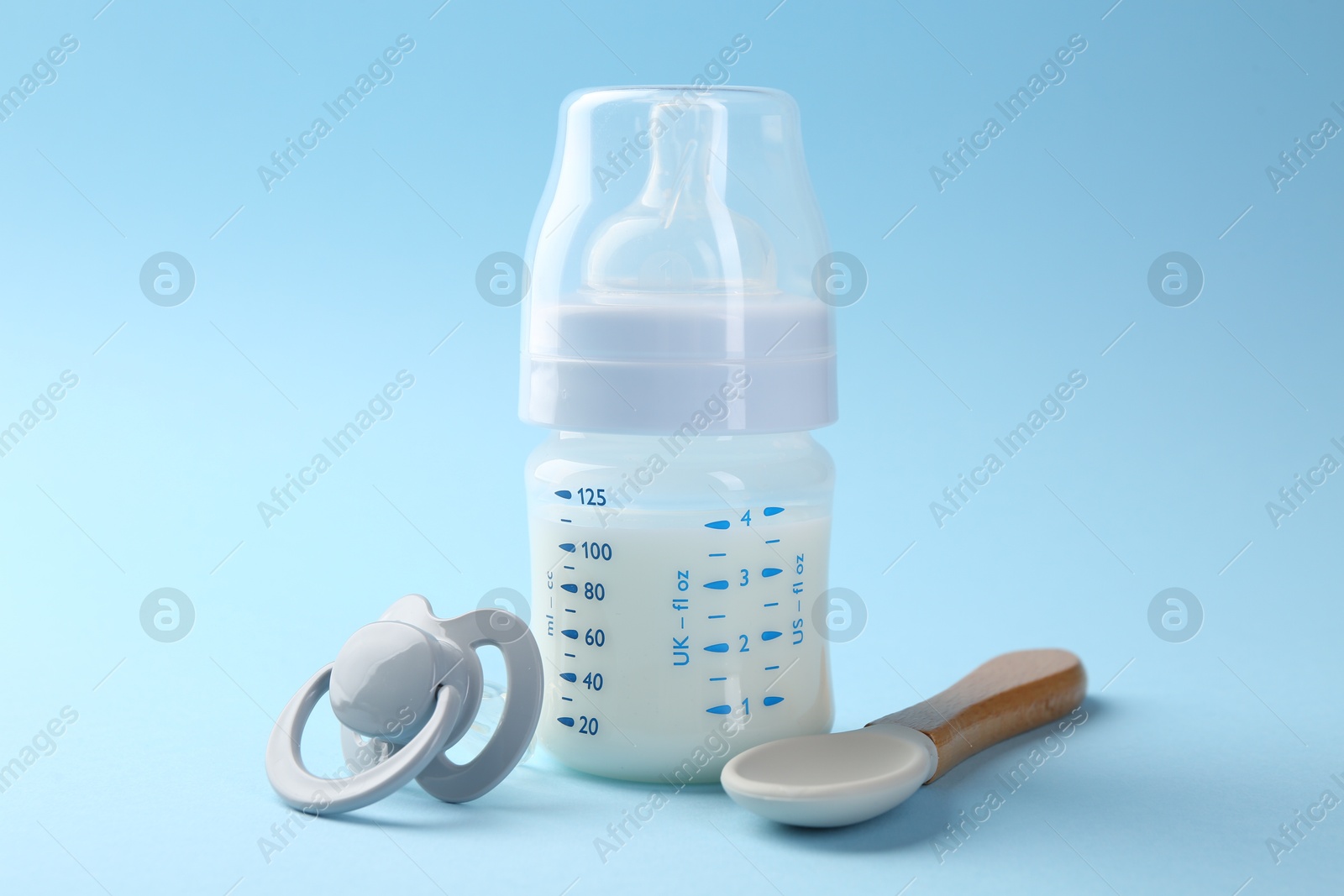 Photo of Feeding bottle with milk, spoon and pacifier on light blue background